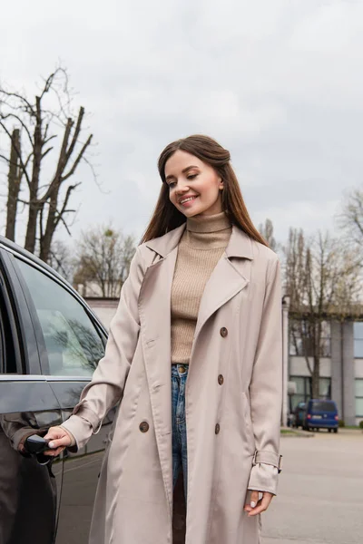 Mujer feliz en gabardina abriendo la puerta del automóvil - foto de stock