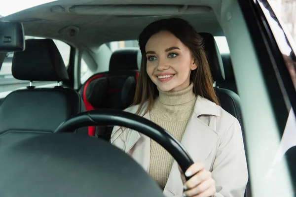 Mujer bastante joven sonriendo mientras conduce un automóvil en la ciudad - foto de stock