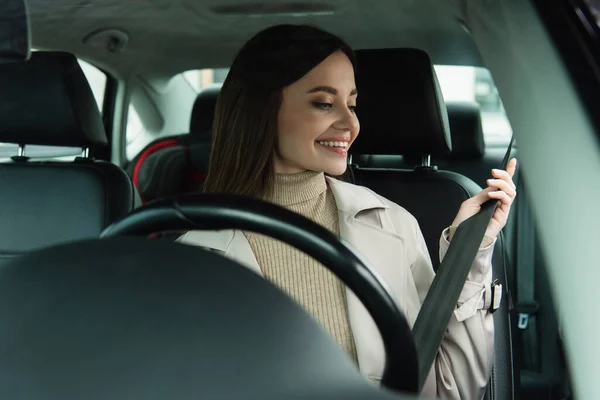 Jeune femme ajustant la ceinture de sécurité tout en étant assis dans la voiture — Photo de stock