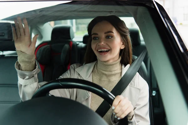 Joyful woman waving hand while driving automobile — Stock Photo