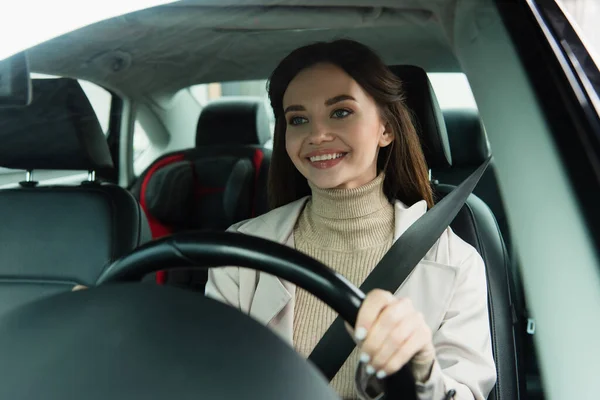 Femme heureuse conduisant l'automobile en ville sur le premier plan flou — Photo de stock