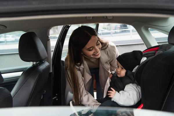 Joyeuse femme regardant bébé garçon assis dans le siège d'auto — Photo de stock