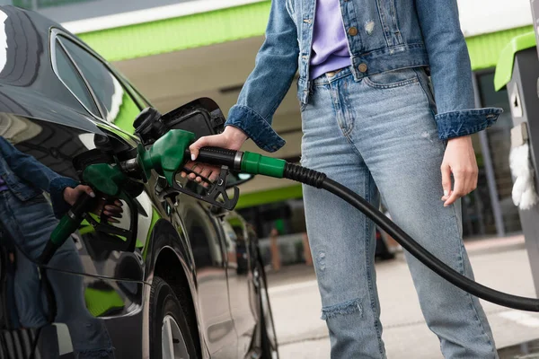 Partial view of woman in jeans refueling automobile on gas station — Stock Photo