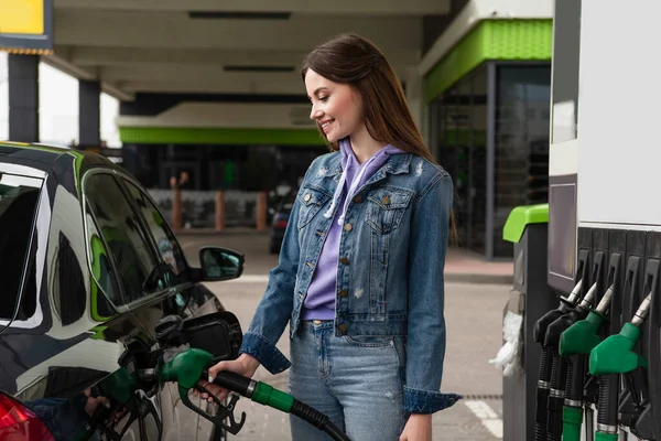 Mulher sorrindo em roupas jeans abastecendo carro no posto de gasolina — Fotografia de Stock