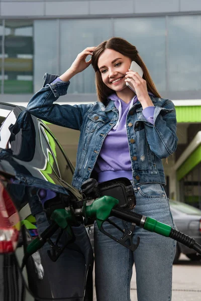 Femme gaie parlant sur téléphone portable tout en rechargeant la voiture sur la station-service — Photo de stock