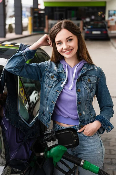 Junge Frau lächelt in Kamera, während sie Auto an Tankstelle betankt — Stockfoto