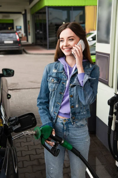 Fröhliche Frau in Jeanskleidung telefoniert an Tankstelle — Stockfoto