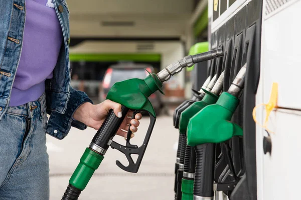 Vista cortada da mulher em roupas jeans segurando pistola de combustível no posto de gasolina — Fotografia de Stock