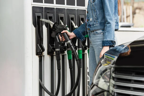 Vue partielle de la femme en denim près des pistolets à essence et de la voiture floue sur la station-service — Photo de stock