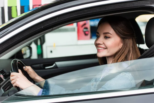 Mujer sonriente mirando a través de la ventana lateral mientras conduce el coche - foto de stock