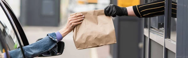 Частичное представление водителя, принимающего еду на вынос от продавца в латексной перчатке, баннер — стоковое фото
