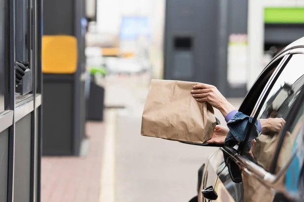 Vista parcial de la mujer en el coche sosteniendo bolsa de papel con comida para llevar - foto de stock