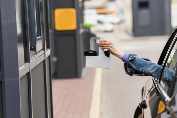 Vista ritagliata della donna in automobile che tiene tazze usa e getta con bevanda da asporto — Foto stock