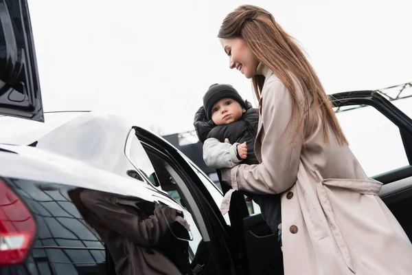 Vue à angle bas de la jeune femme tenant tout-petit fils près de la voiture — Photo de stock