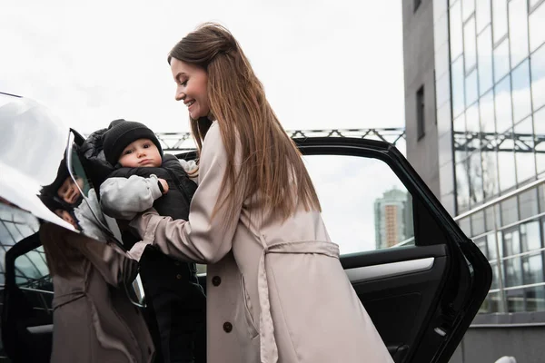 Bonita mujer poniendo hijo pequeño en el coche - foto de stock