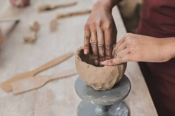 Vista parziale di giovane donna afroamericana scolpire vaso di argilla con le mani in ceramica — Foto stock