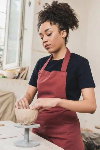 Сфокусированная молодая африканская американка, создающая глиняный горшок руками в керамике — стоковое фото