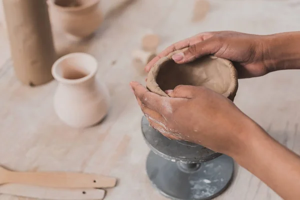 Vue partielle de jeune femme afro-américaine sculptant pot d'argile avec les mains en poterie — Photo de stock