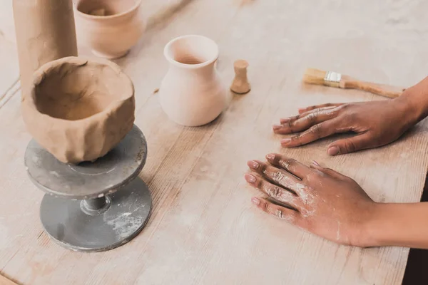 Vue grand angle du pot d'argile fait main sur la table près des mains de la jeune femme afro-américaine en poterie — Photo de stock