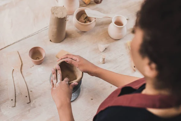 Vista ad alto angolo di giovane donna afro-americana scolpire vaso di argilla con le mani in ceramica — Foto stock