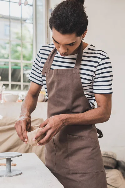 Concentrado joven afroamericano hombre esculpir olla de arcilla con las manos en la cerámica — Stock Photo