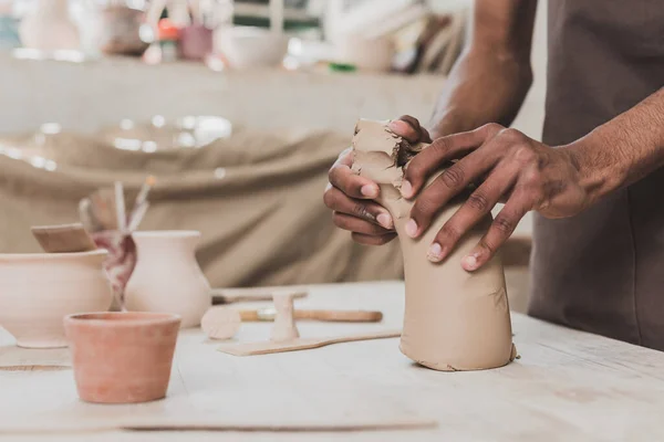 Visão parcial do jovem afro-americano trabalhando com pedaço de argila na mesa com equipamentos em cerâmica — Fotografia de Stock