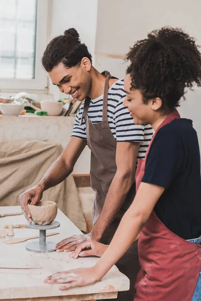 Smiling young african american couple sculpting clay pot in pottery — Stock Photo