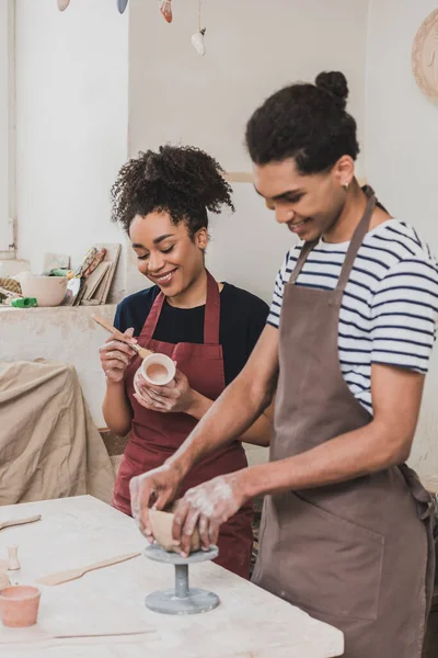 Smiling young african american man and woman sculpting clay pot in pottery — Stock Photo