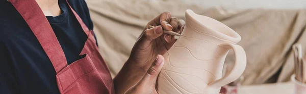 Partial view of young african american woman sculpting clay pot with stick in pottery, banner — Stock Photo