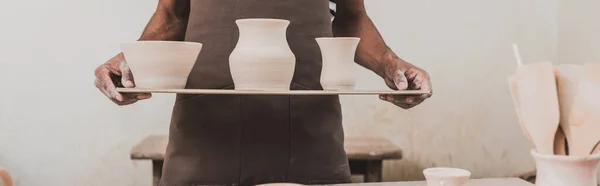 Visão parcial do jovem afro-americano de pé com vasos de barro na bandeja, banner — Fotografia de Stock