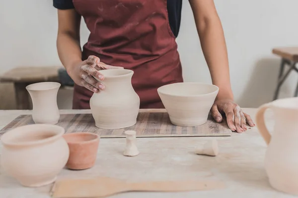 Partial view of young african american woman touching clay pot on tray in pottery — Stock Photo