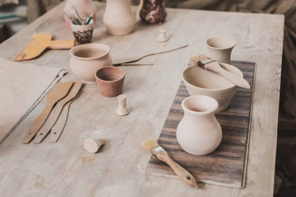 Vista ad alto angolo di vasi di argilla fatti a mano su tavolo di legno vicino alle attrezzature in ceramica — Foto stock