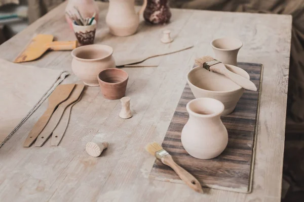 High angle view of handmade clay pots on wooden table near equipment in pottery — Stock Photo