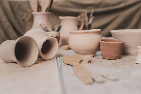 Глиняные горшки ручной работы и керамическое оборудование на деревянном столе в художественной студии — стоковое фото