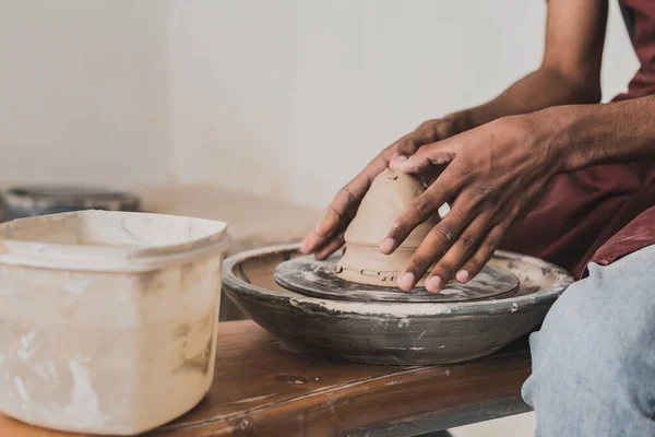 Partial view of young african american man modeling wet clay on wheel in pottery — Stock Photo