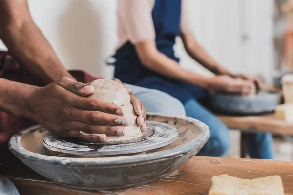 Partial view of young african american couple modeling wet clay on wheels in pottery — Stock Photo