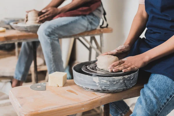 Partial view of young african american couple in aprons modeling wet clay on wheels in pottery — Stock Photo