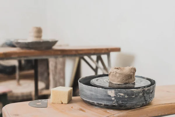 Pedazo mojado de arcilla en la rueda de cerámica y esponja en el banco de madera en el estudio de arte - foto de stock