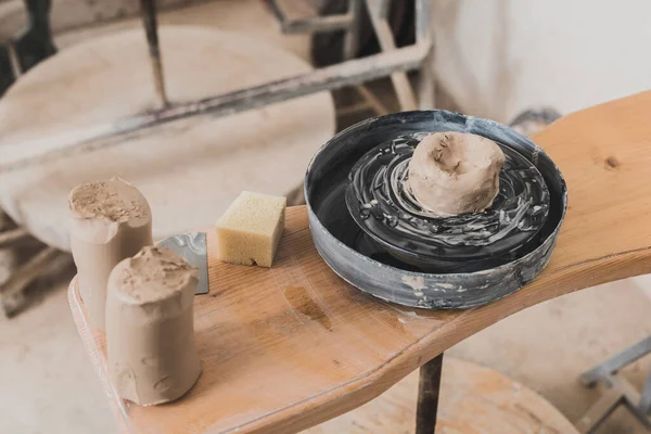 Visão de alto ângulo de peça molhada de argila na roda de cerâmica e esponja no banco de madeira no estúdio de arte — Fotografia de Stock