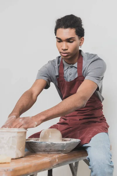 Серйозний молодий афроамериканський чоловік миє руки в пластиковій коробці біля мокрої глини на колесі в кераміці — стокове фото