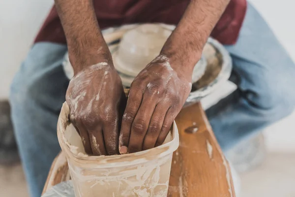 Vista parziale di giovane uomo africano americano lavarsi le mani in scatola di plastica vicino argilla bagnata su ruota in ceramica — Foto stock