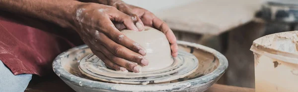 Partial view of young african american man modeling wet clay on wheel in pottery, banner — Stock Photo