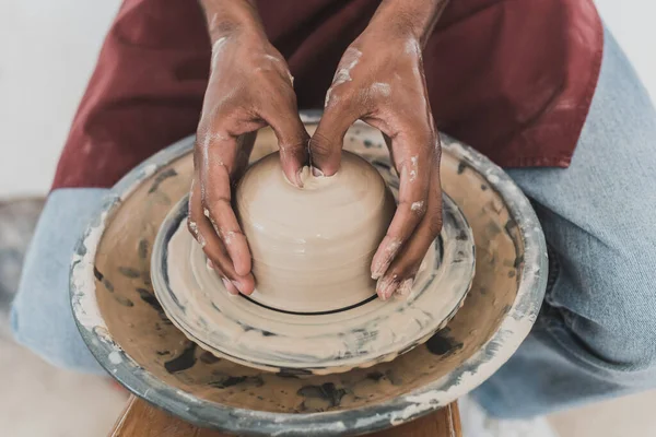 Close up view of young african american man modeling wet clay on wheel with hands in pottery — Stock Photo