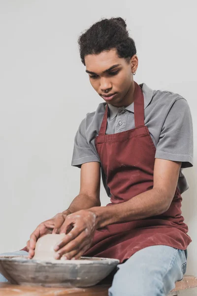 Serious young african american man modeling wet clay on wheel with hands in pottery — Stock Photo