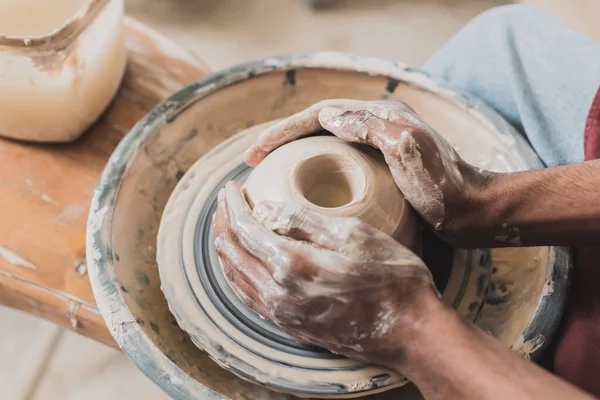 Close up view of young african american man modeling wet clay on wheel with hands in pottery — Stock Photo