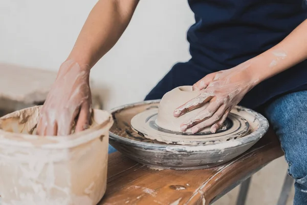 Partial view of young african american woman modeling wet clay on wheel and washing hand in plastic box in pottery — Stock Photo