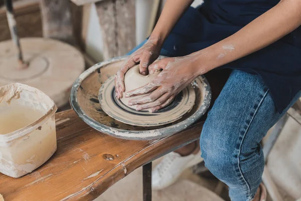 Partial view of young african american woman modeling wet clay on wheel with hands in pottery — Stock Photo