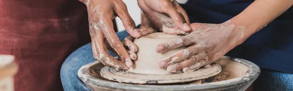 Partial view of young african american couple modeling wet clay on wheel with hands in pottery, banner — Stock Photo