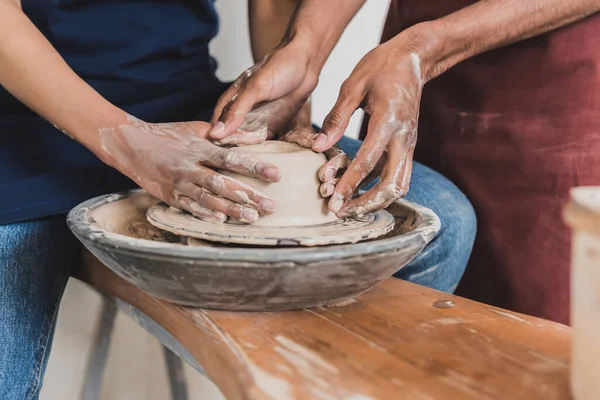 Partial view of young african american couple modeling wet clay on wheel with hands in pottery — Stock Photo