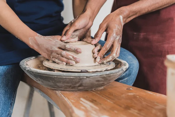 Vue partielle du jeune couple afro-américain modelant de l'argile humide sur roue avec les mains en poterie — Photo de stock